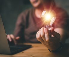 Woman hand holding light bulb and using laptop on wooden table. new idea creativity concept with innovation and inspiration