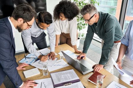 Diverse international executive business people group brainstorming at boardroom meeting table. Multiethnic team discussing project developing business strategy doing paperwork analysis in office.
